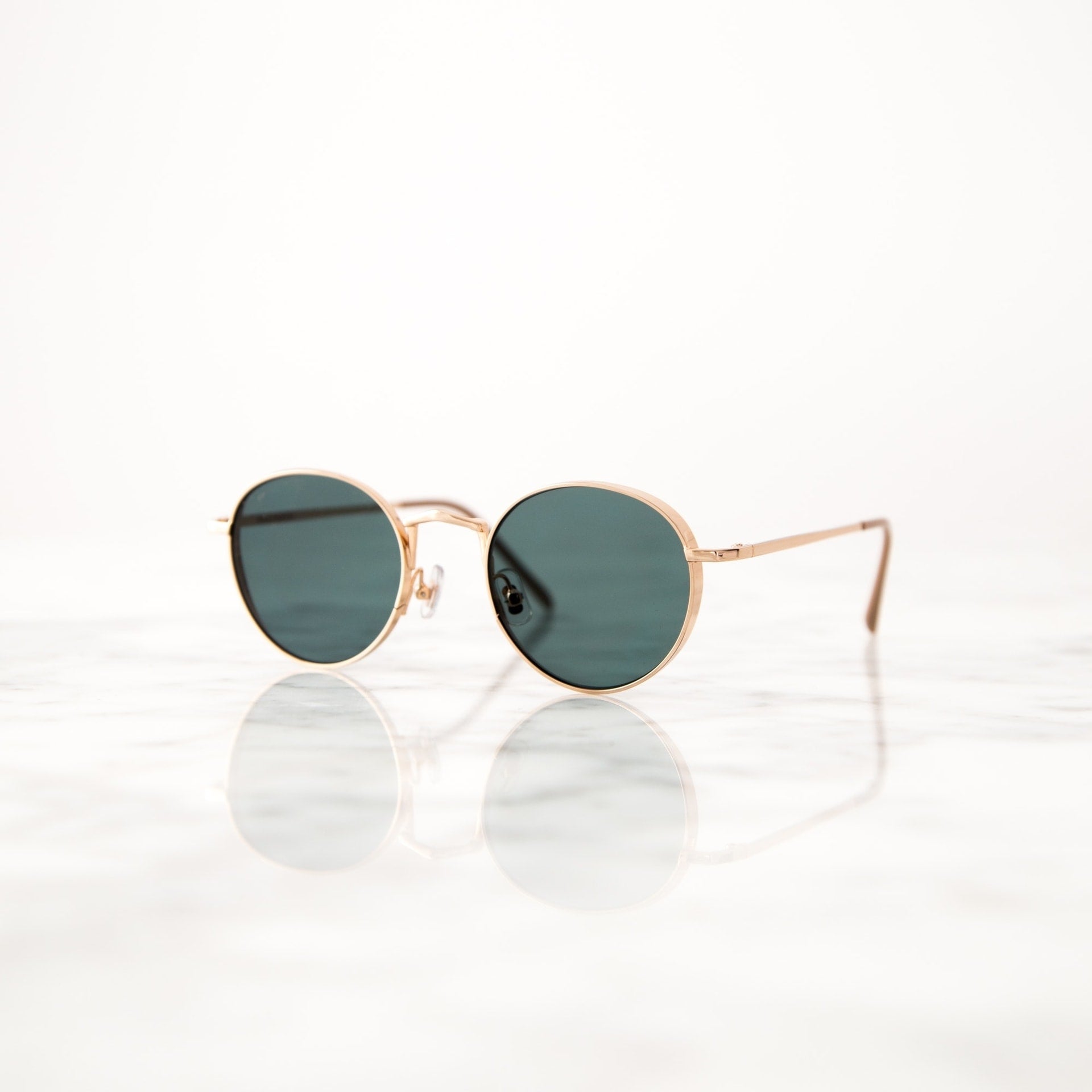 Lunettes de soleil à monture dorée sur surface réfléchissante en marbre